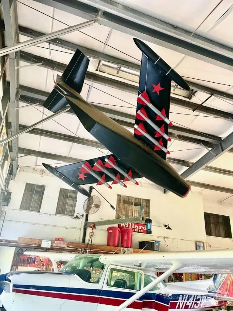 A black model aircraft with red stars and missiles, hanging above a white and blue light aircraft in a hangar.