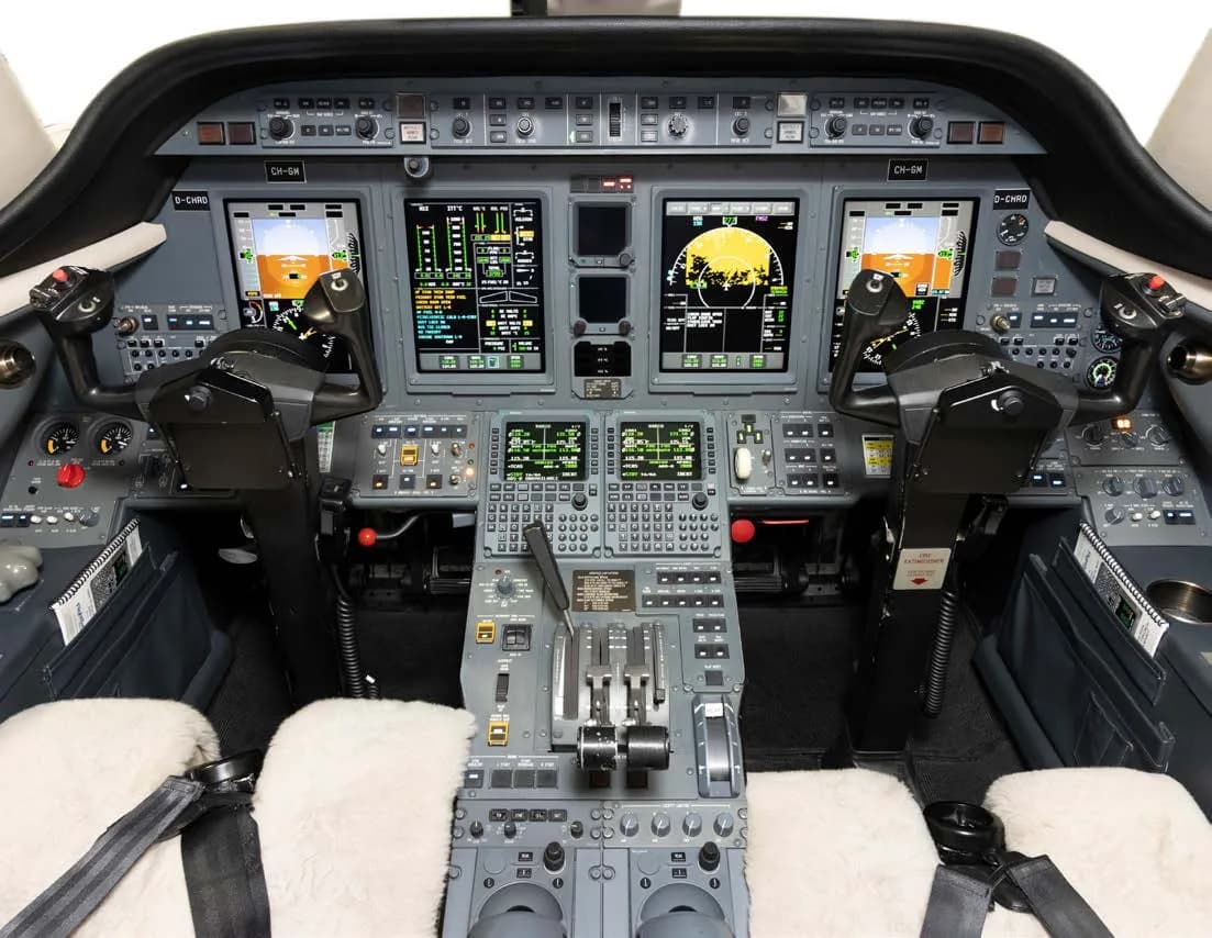 The cockpit of a business jet, featuring multiple digital displays and control yokes with sheepskin covers.