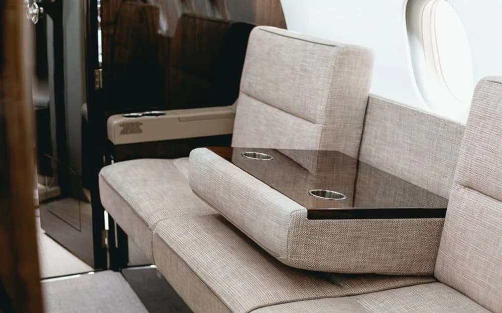 A close-up of a beige fabric divan in the Dassault Falcon 900EX cabin, with a fold-out table featuring cup holders.