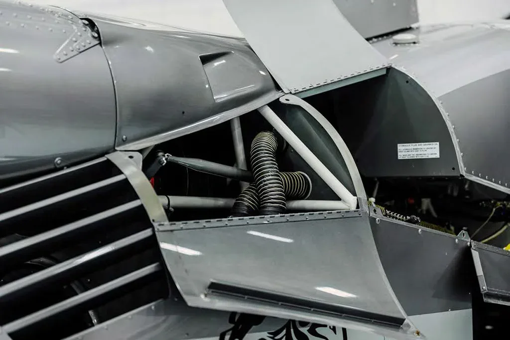 An open panel on the side of a grey helicopter revealing internal components and hoses.