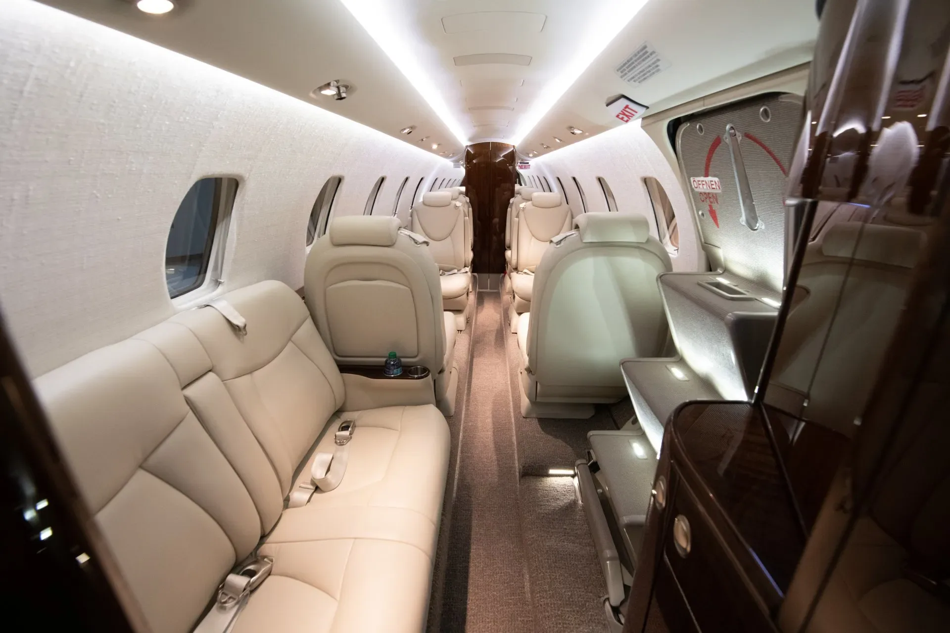 A view down the aisle of a business jet cabin with cream-colored leather seats.
