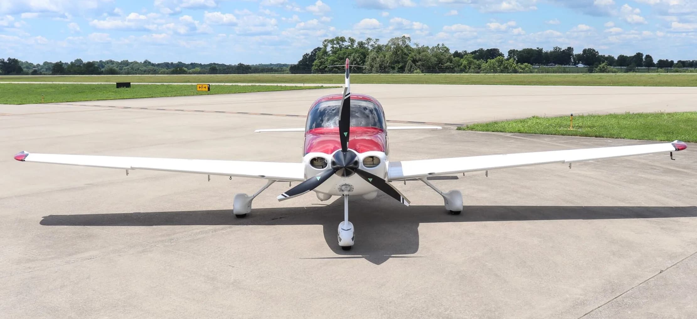 A front view of a white and red single-engine aircraft with its doors closed, parked on an airfield.