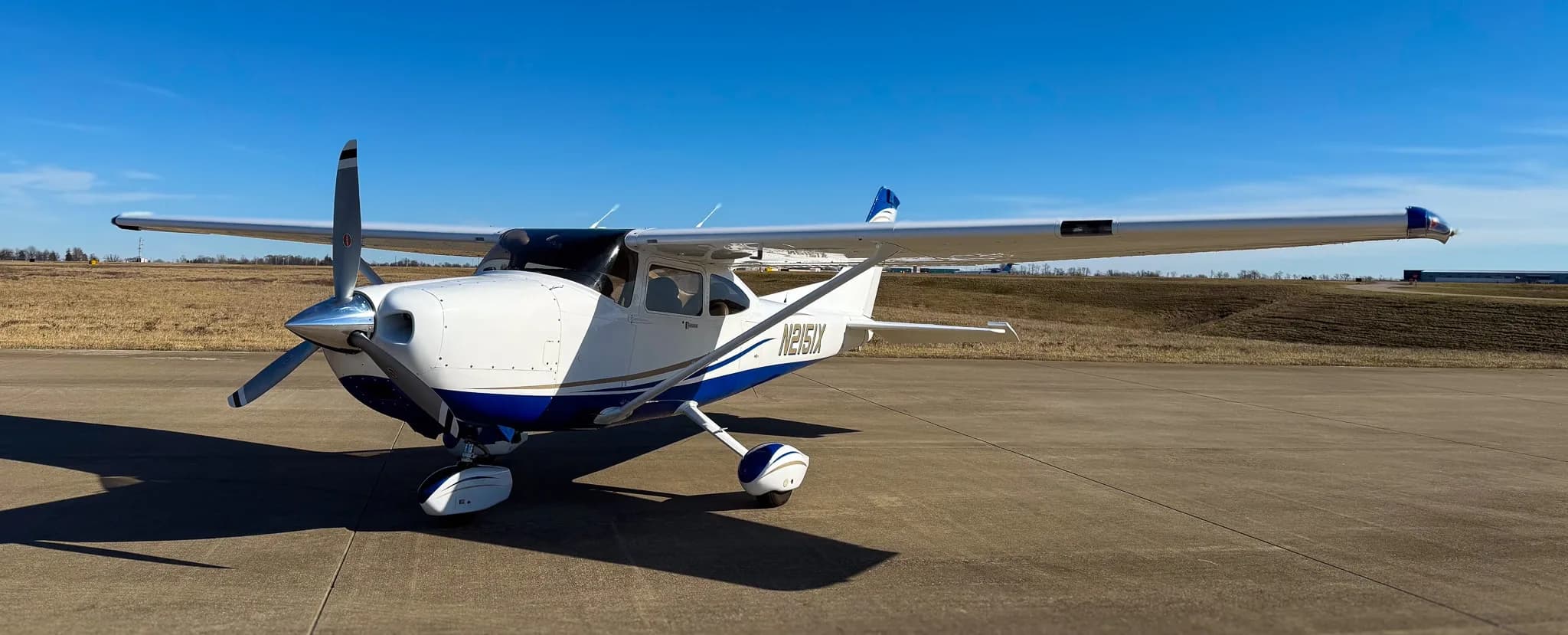 A white and blue Cessna 182 Skylane (N2151X) parked on a tarmac, viewed from the front.