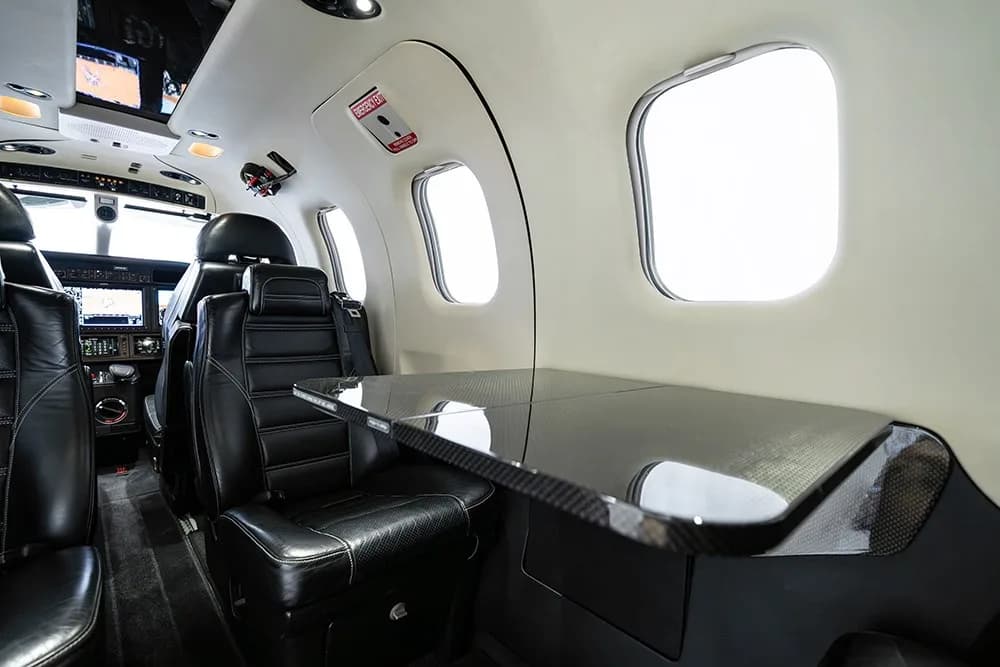 A view of the TBM 930 cabin showing black leather seats and a carbon fiber fold-out table.