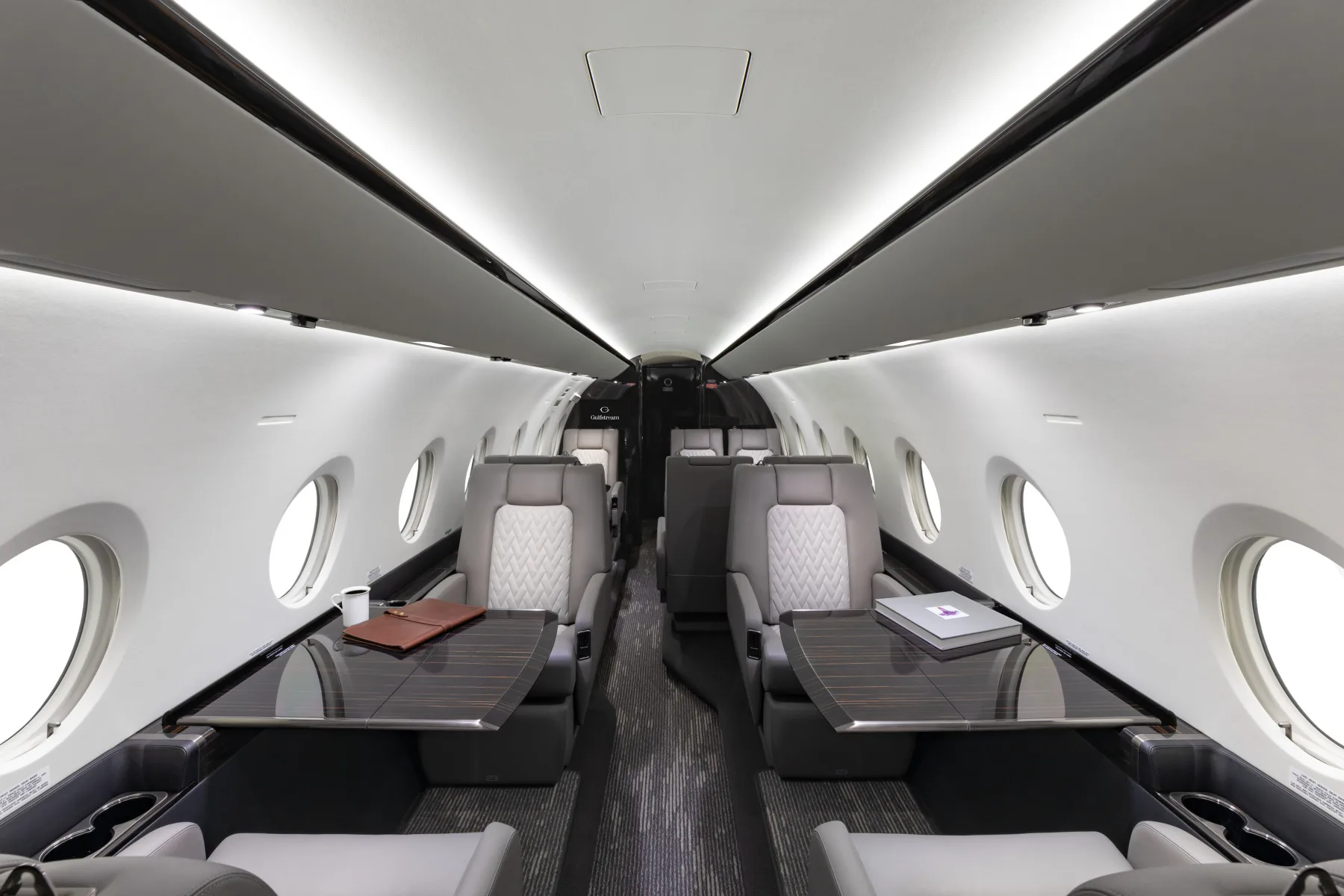 Forward view of the aircraft cabin with leather seats and oval windows, with tables extended.