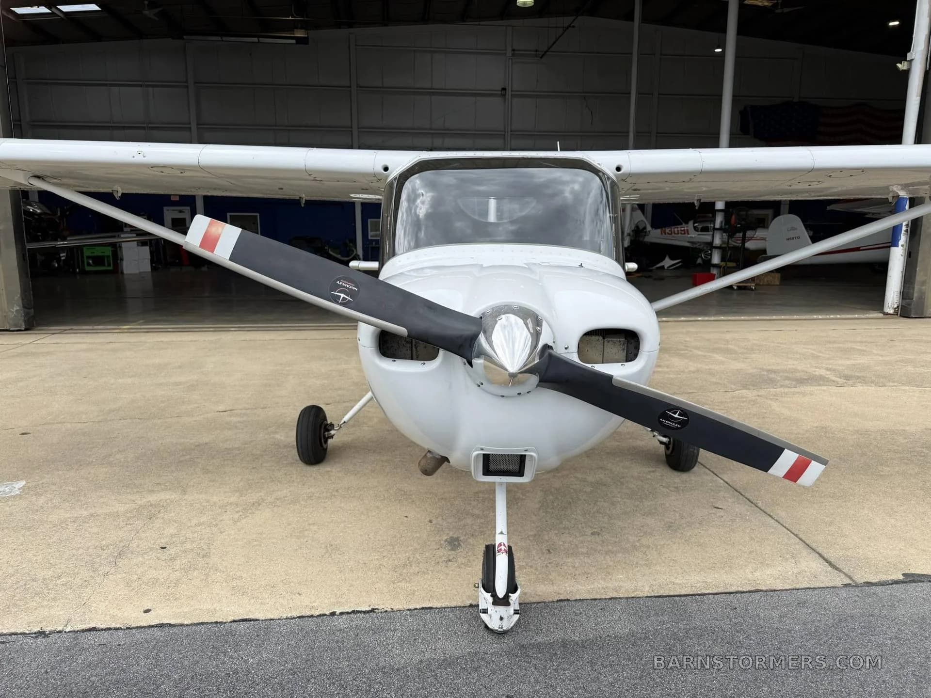 A white Cessna Skycatcher light-sport aircraft with a black propeller, viewed head-on, parked outside a hangar.