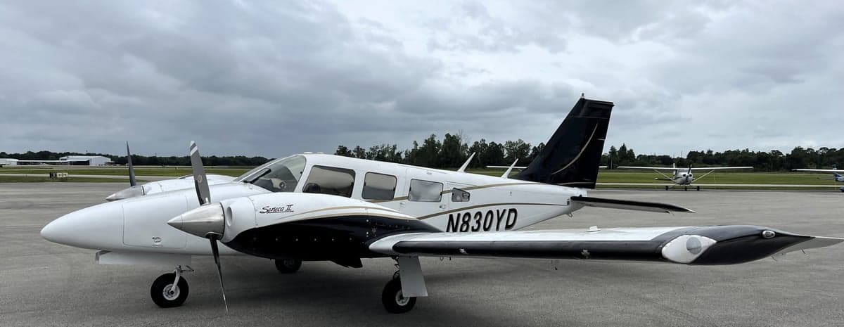A Piper Seneca II aircraft with a white and black paint scheme is parked on the tarmac.