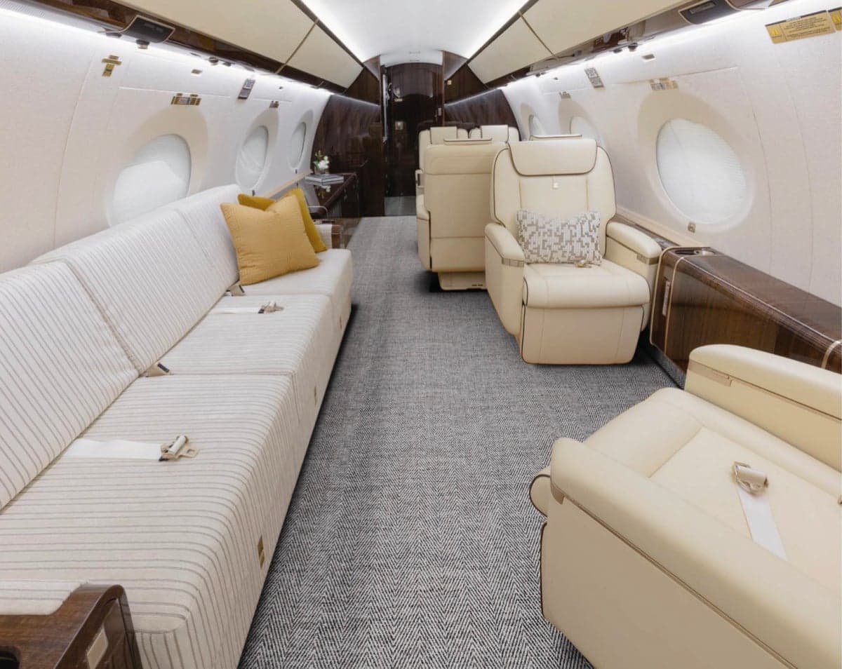 Aircraft cabin with a sofa, cream-colored leather seats, and gray carpet.
