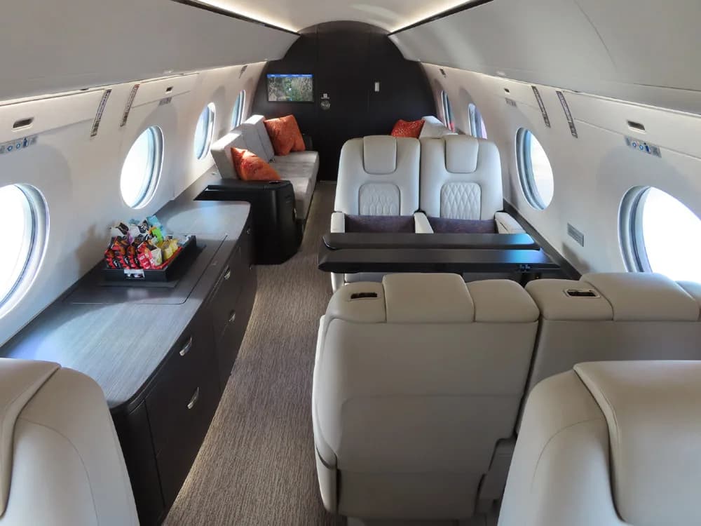 Aircraft cabin with leather seats, a couch, and a snack tray.