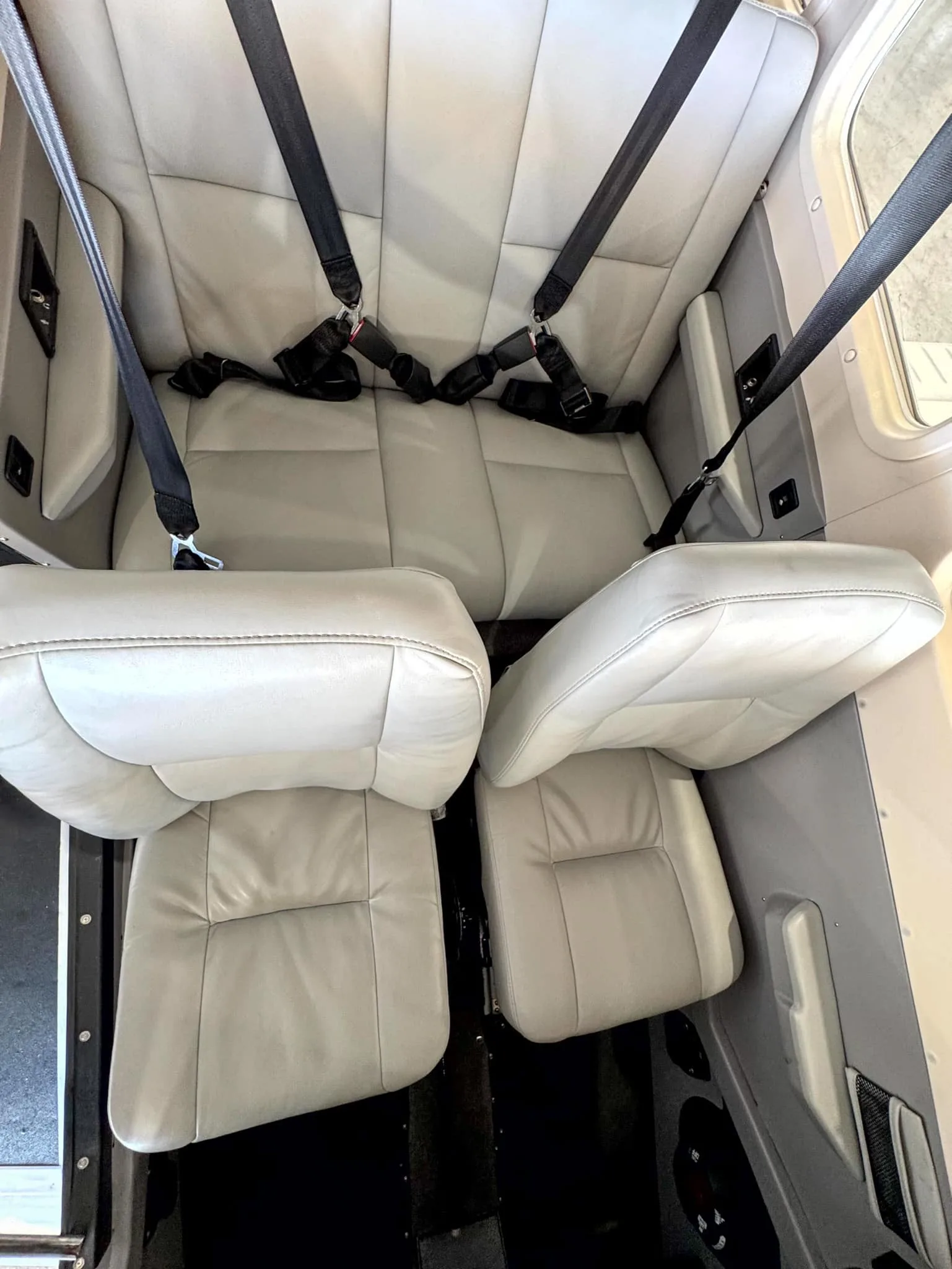 An overhead view of the light gray leather rear seats with black seatbelts in the aircraft cabin.