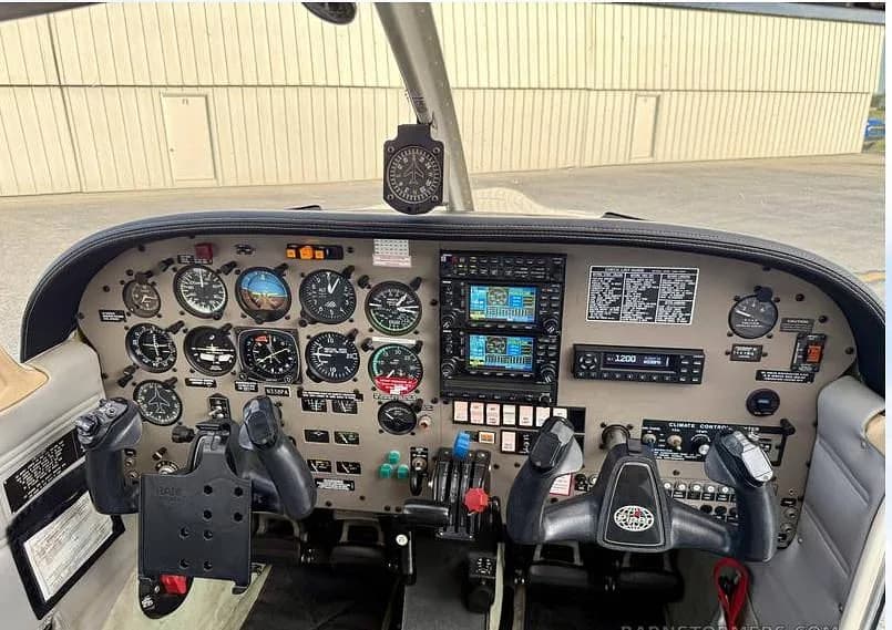 The cockpit of a Piper Arrow aircraft, showing the instrument panel with analog gauges, two Garmin GNS 430 units, and control yokes.