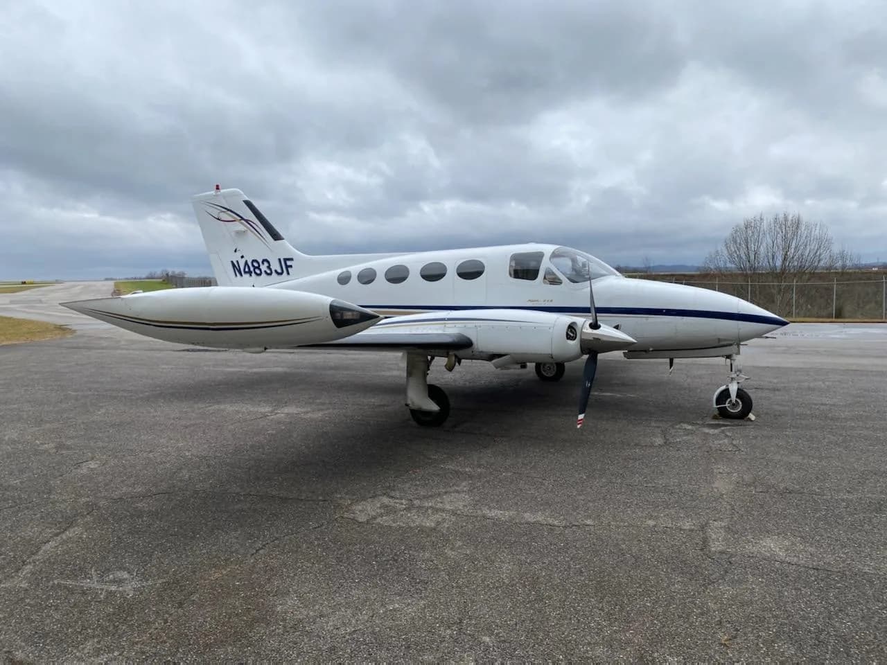 A white and blue Cessna 414 Chancellor, registration N483JF, parked on an asphalt apron under a cloudy sky.