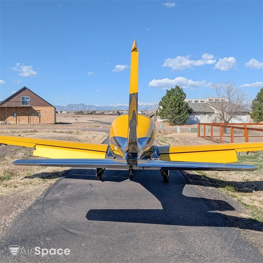 A rear view of a yellow and black Freccia F200 aircraft with a distinctive tail, parked on an asphalt ramp.