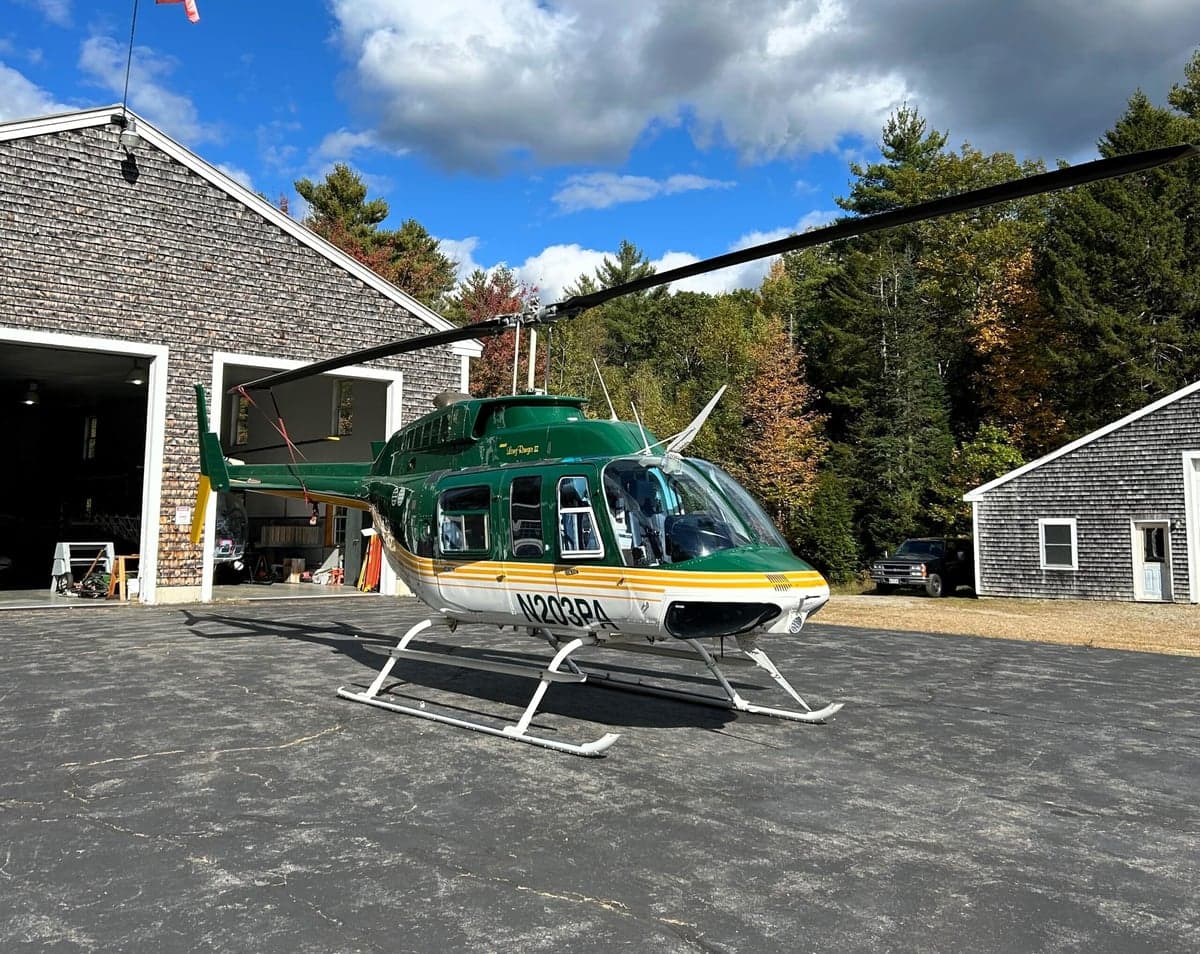 A green and white Bell 206 helicopter parked outside a hangar.