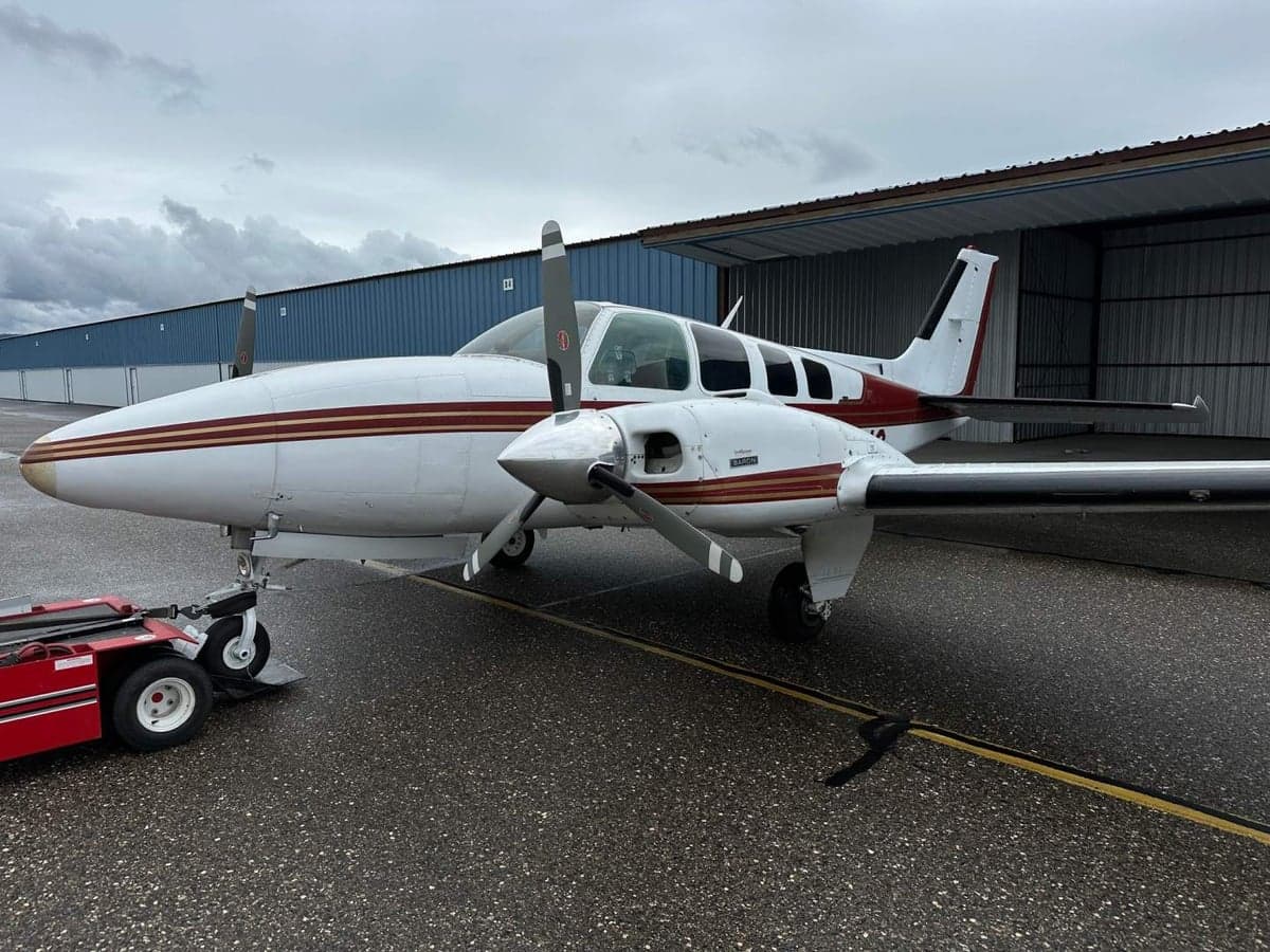A Beechcraft Baron aircraft with a white and maroon paint scheme is parked on the tarmac.