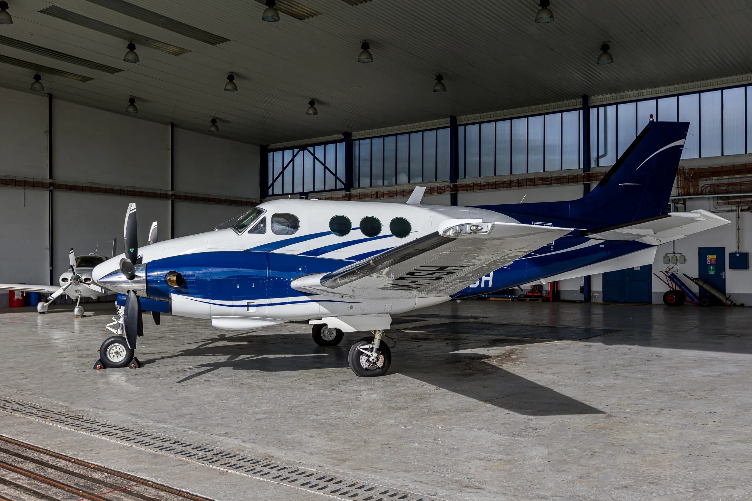 A white and blue twin-engine turboprop aircraft, registration OK-DSH, parked inside a hangar.