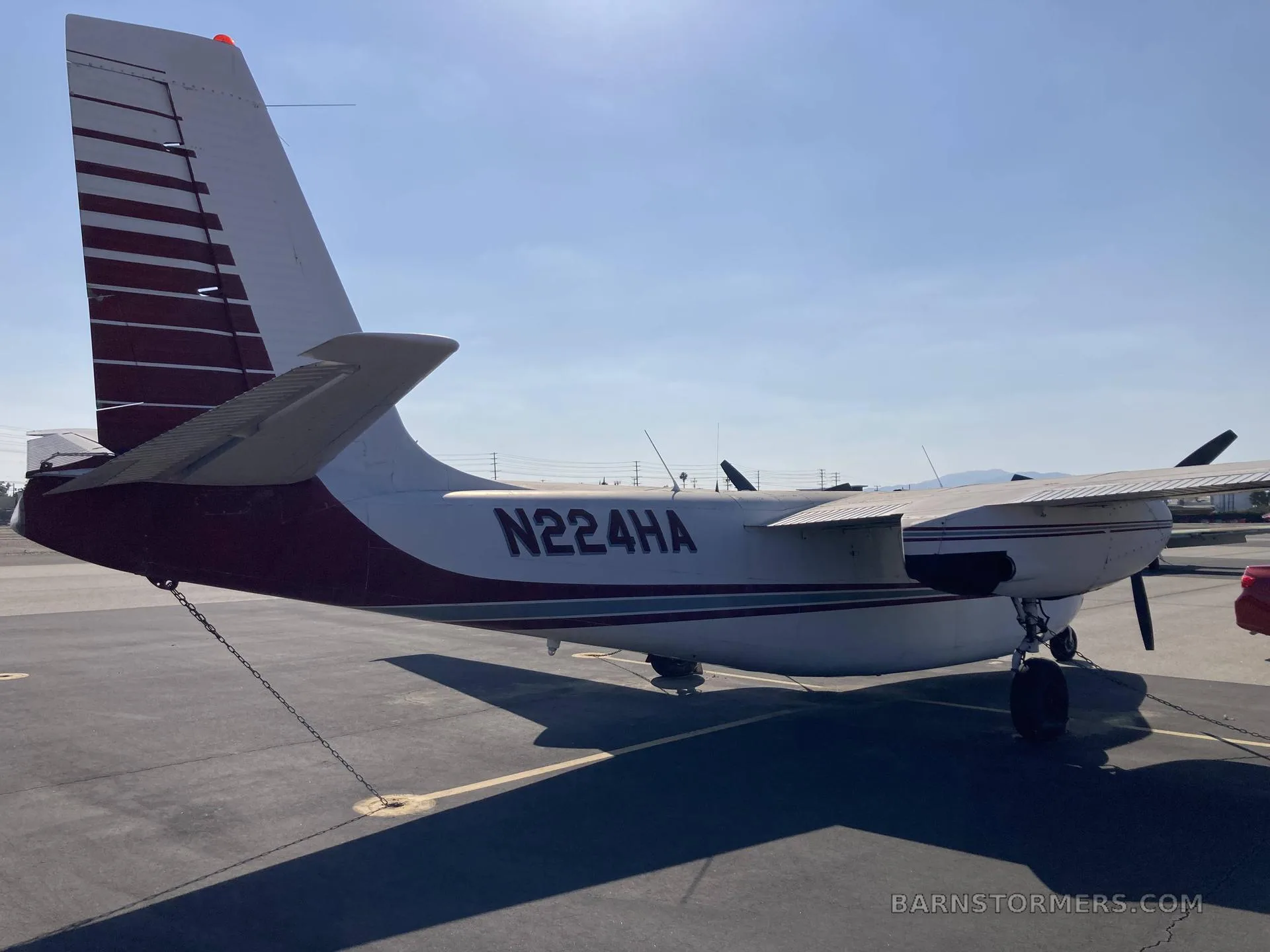 The rear-right view of a white and red twin-engine Commander aircraft (N224HA), showing the tail and right engine.