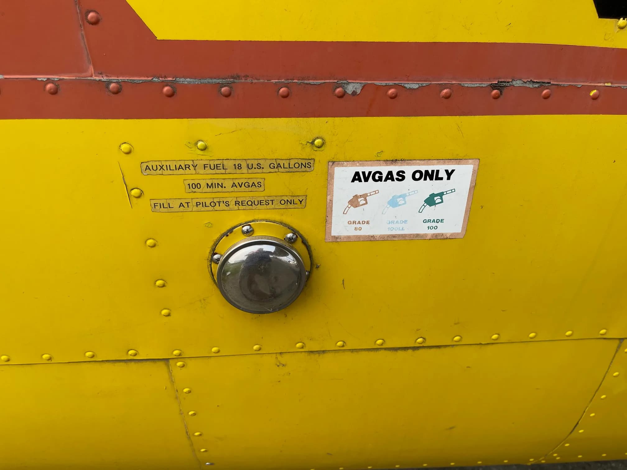 Close-up of the fuel filler and AVGAS ONLY label on a yellow aircraft.