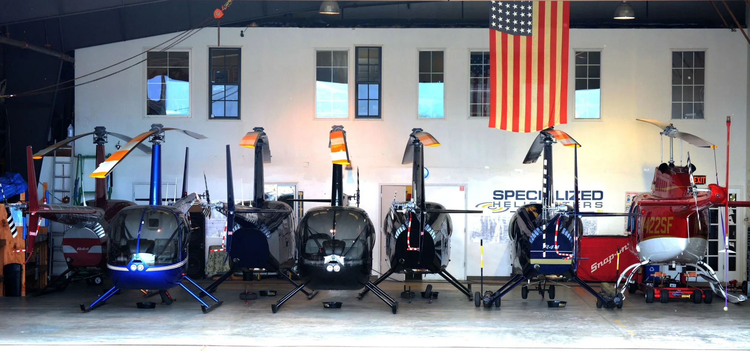 Several helicopters are parked in a hangar with an American flag.