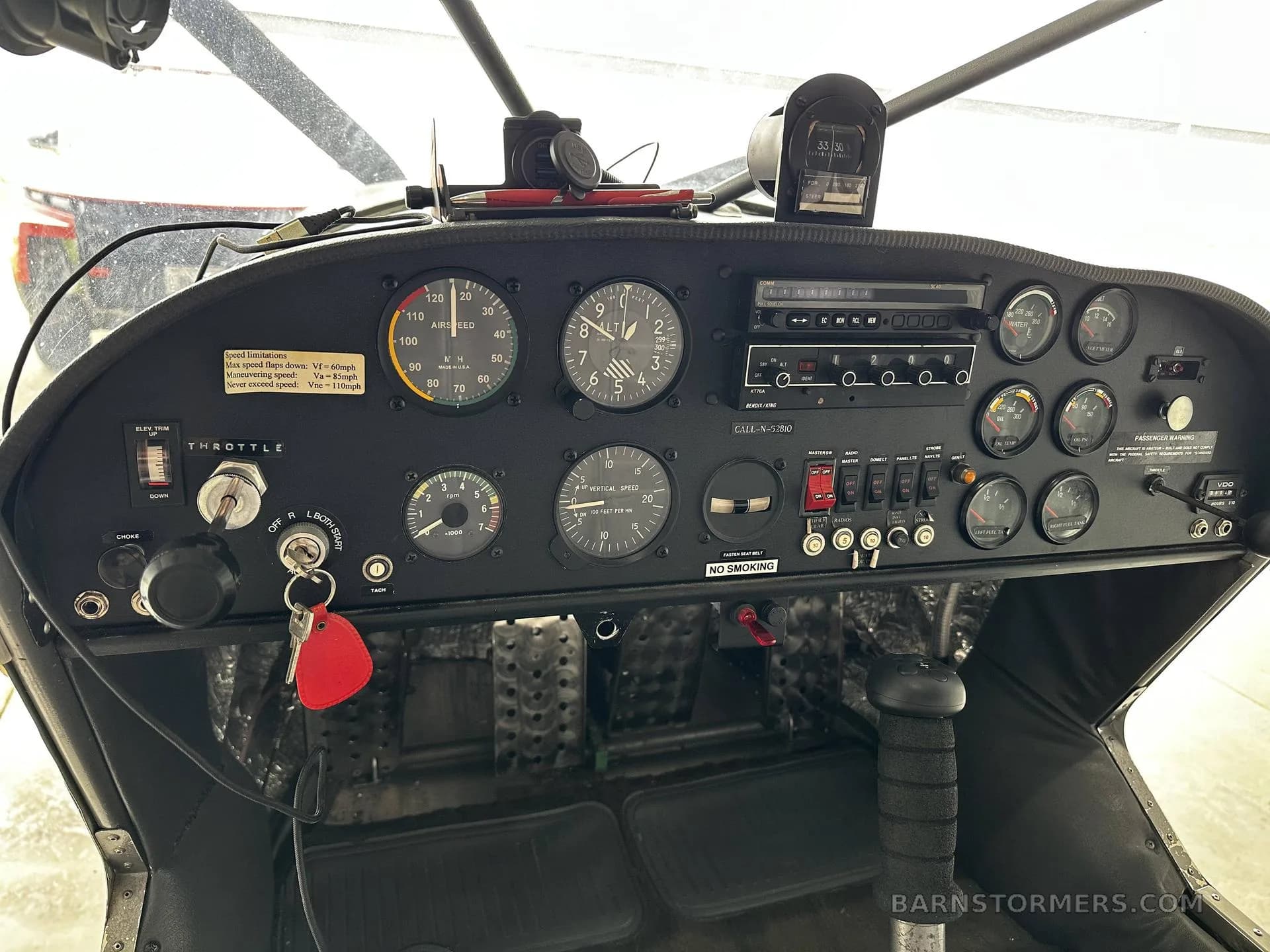 A close-up view of the aircraft's black instrument panel with various gauges, switches, and a radio, showing a red key hanging from the ignition.