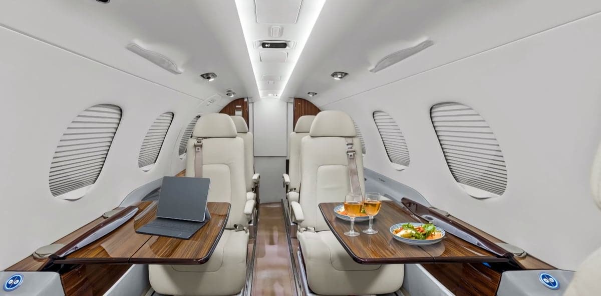 The interior of a Phenom 300 aircraft with tables, seating, and refreshments.
