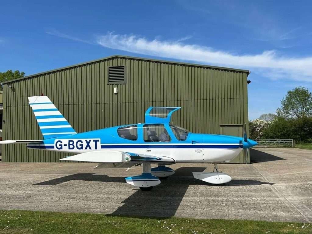 A blue and white aircraft is parked in front of a hangar.