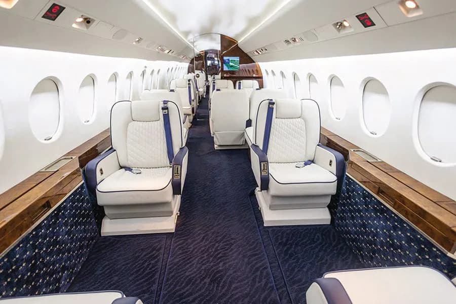 The luxurious cabin interior of a business jet with white and blue quilted seats and dark blue carpet.