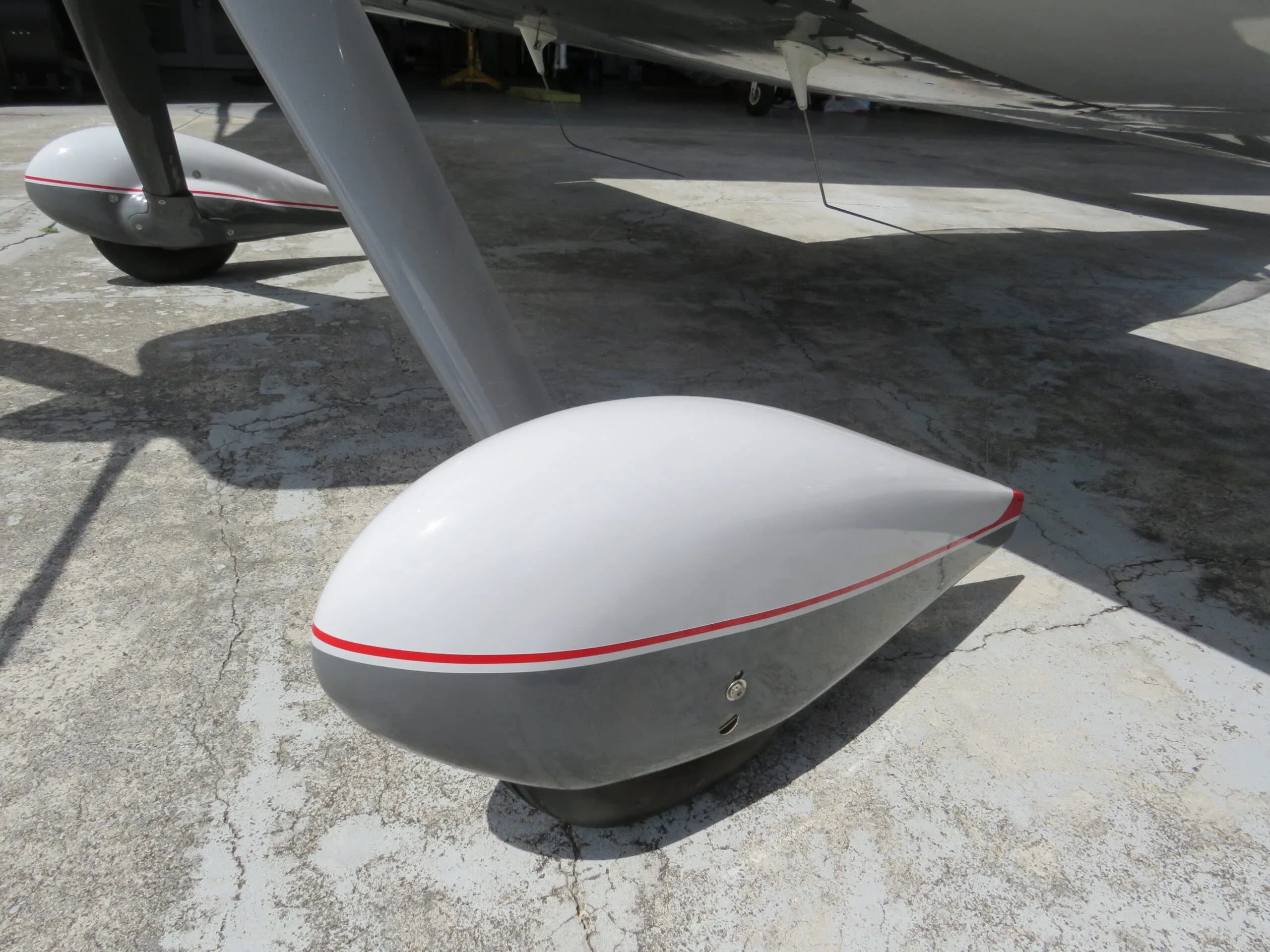 Close-up view of the white and grey main landing gear fairing with a red stripe, on concrete.