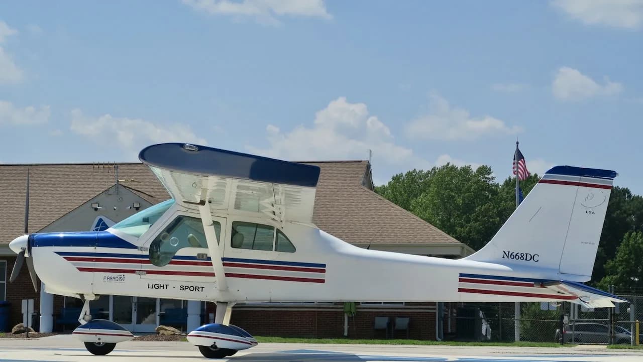 A full side profile of a white Paradise P1 Light Sport aircraft with blue and red stripes, parked on an airfield.