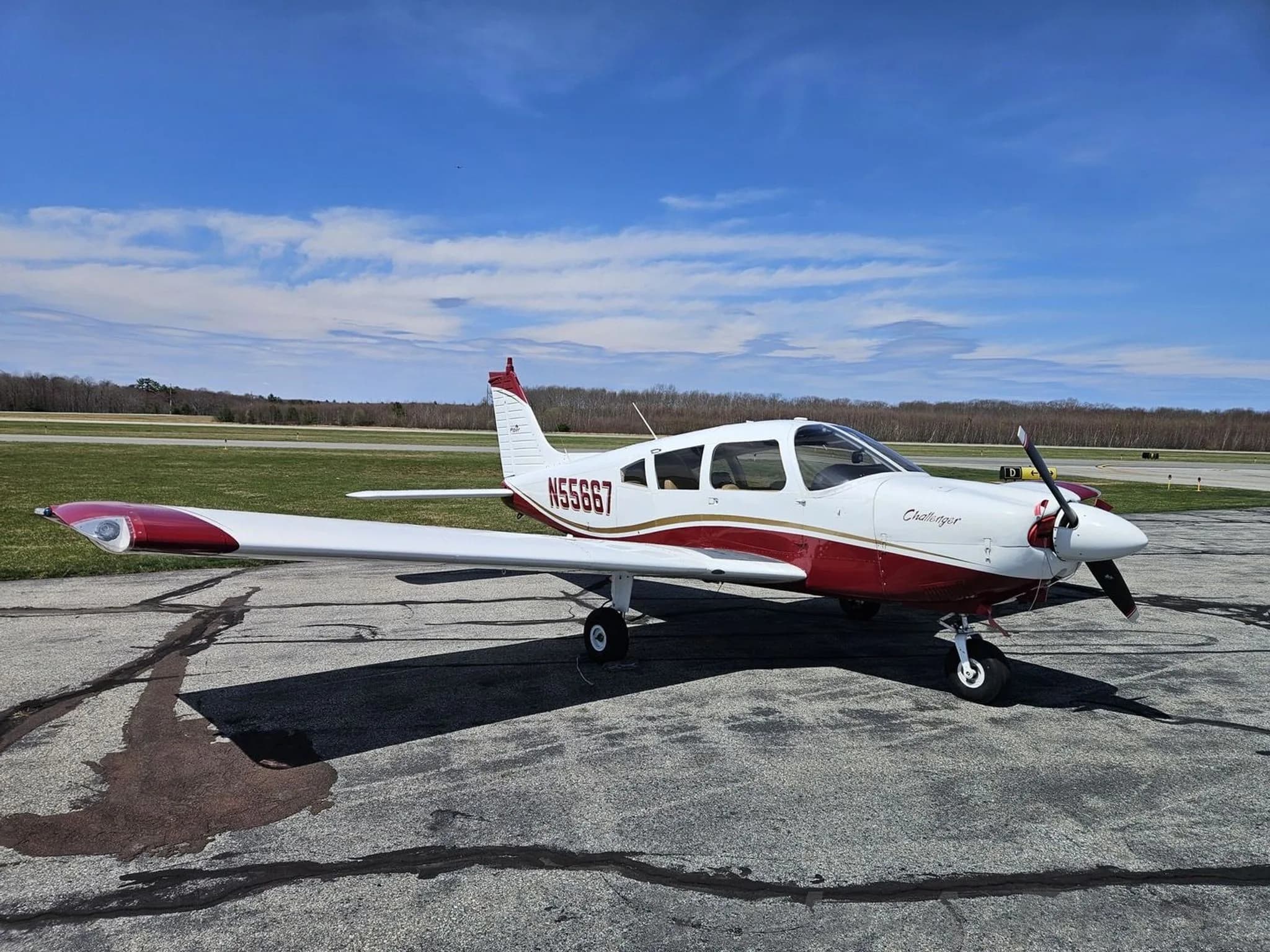 Side view of a white and maroon Piper PA-28 Challenger aircraft with registration N55667 parked on an airfield.
