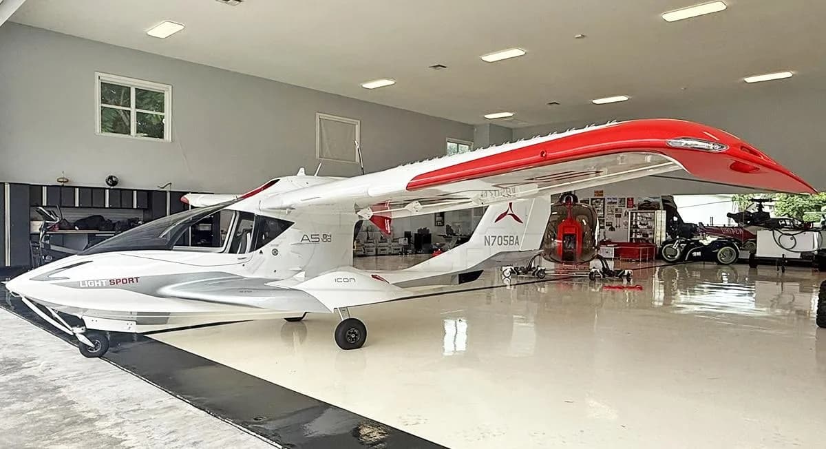 Side view of a white and red Icon A5 amphibious light sport aircraft with wings extended, inside a hangar.