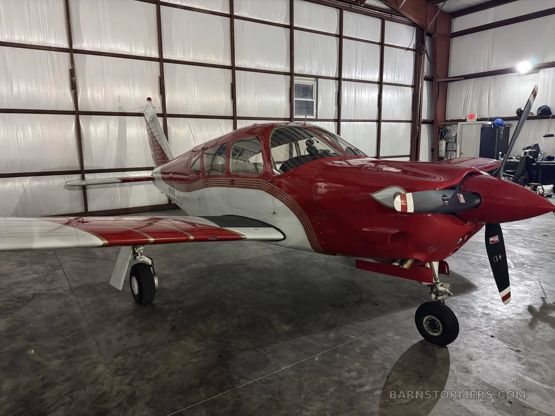 A red and white Mooney M20 series aircraft parked inside a hangar, viewed from the front-right.