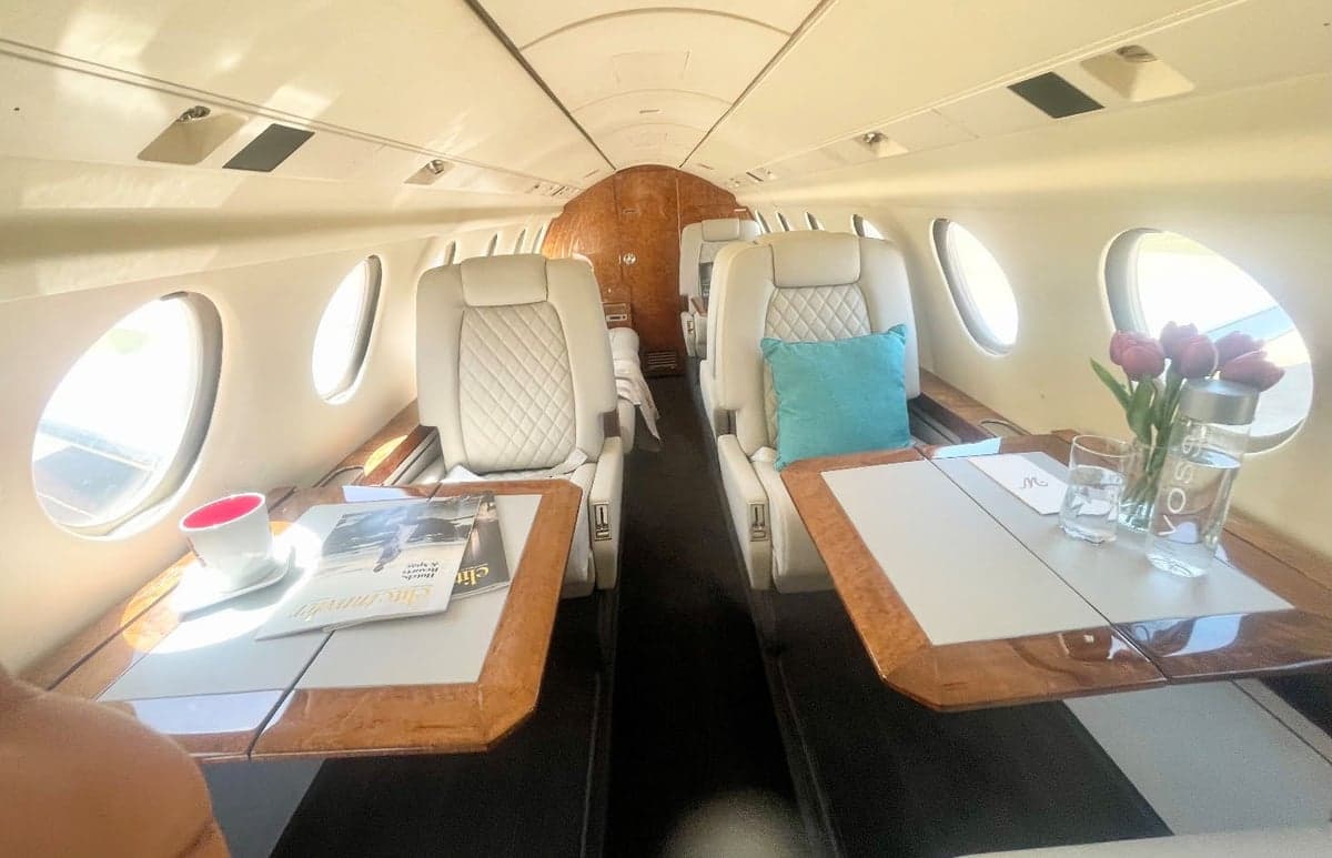 Aircraft interior with white leather seats and wood trim.