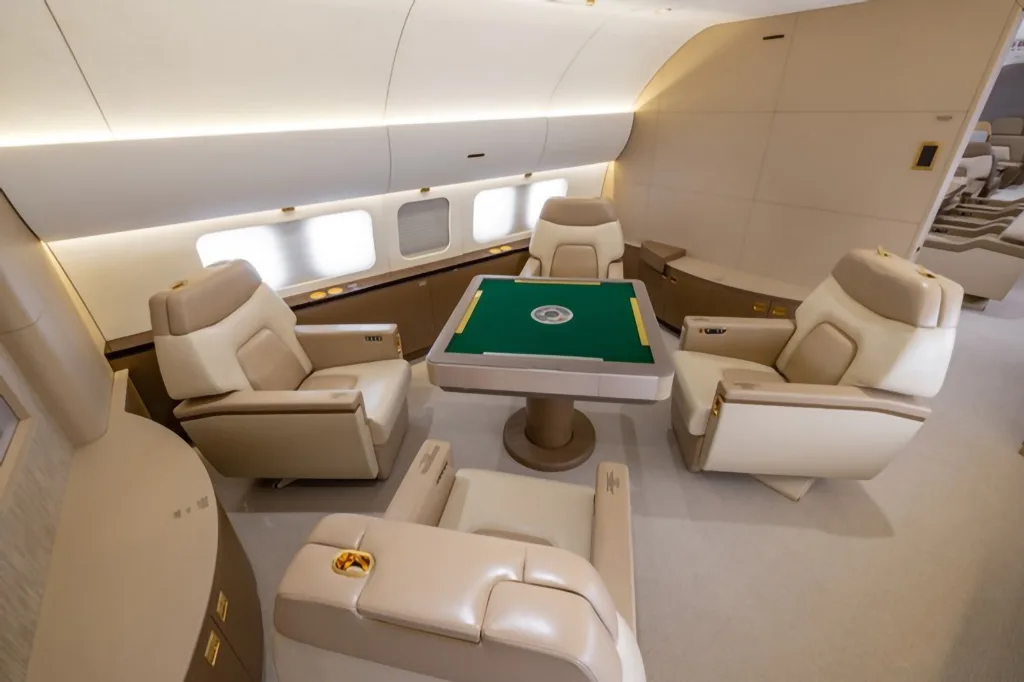 A close-up view of a green-topped game table surrounded by four luxurious beige leather seats in an aircraft cabin.