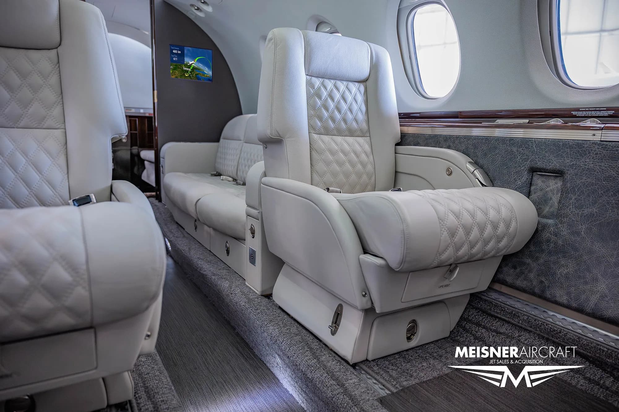 A close-up view of the quilted white leather seats and a side couch in the business jet's cabin.