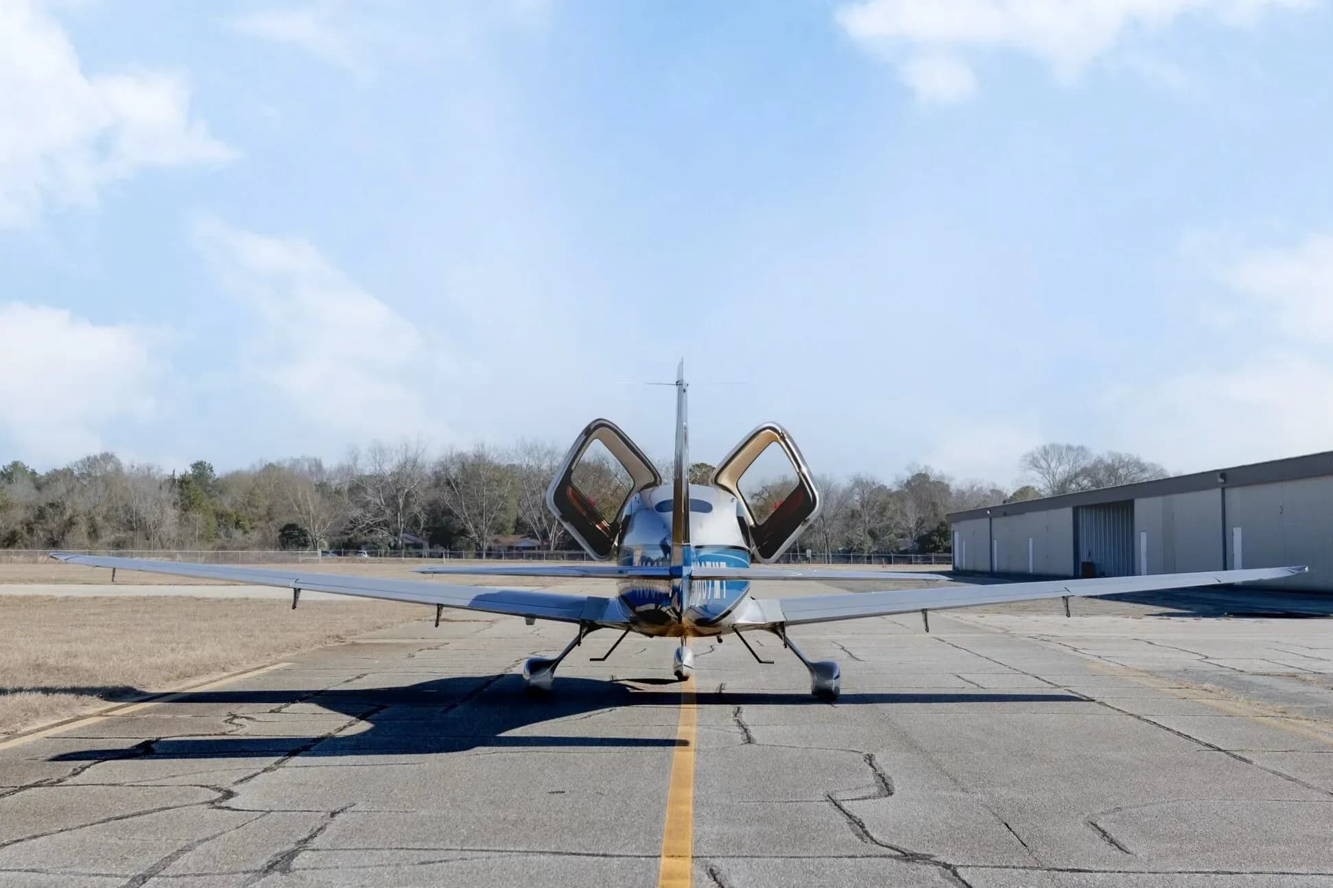A rear view of the Cirrus SR20 GTS aircraft with N667MT registration, showing its open gull-wing doors on an airfield.