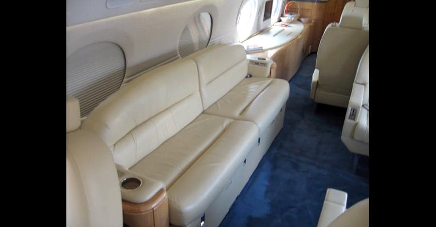 Aircraft interior with cream-colored leather seats and blue carpet.