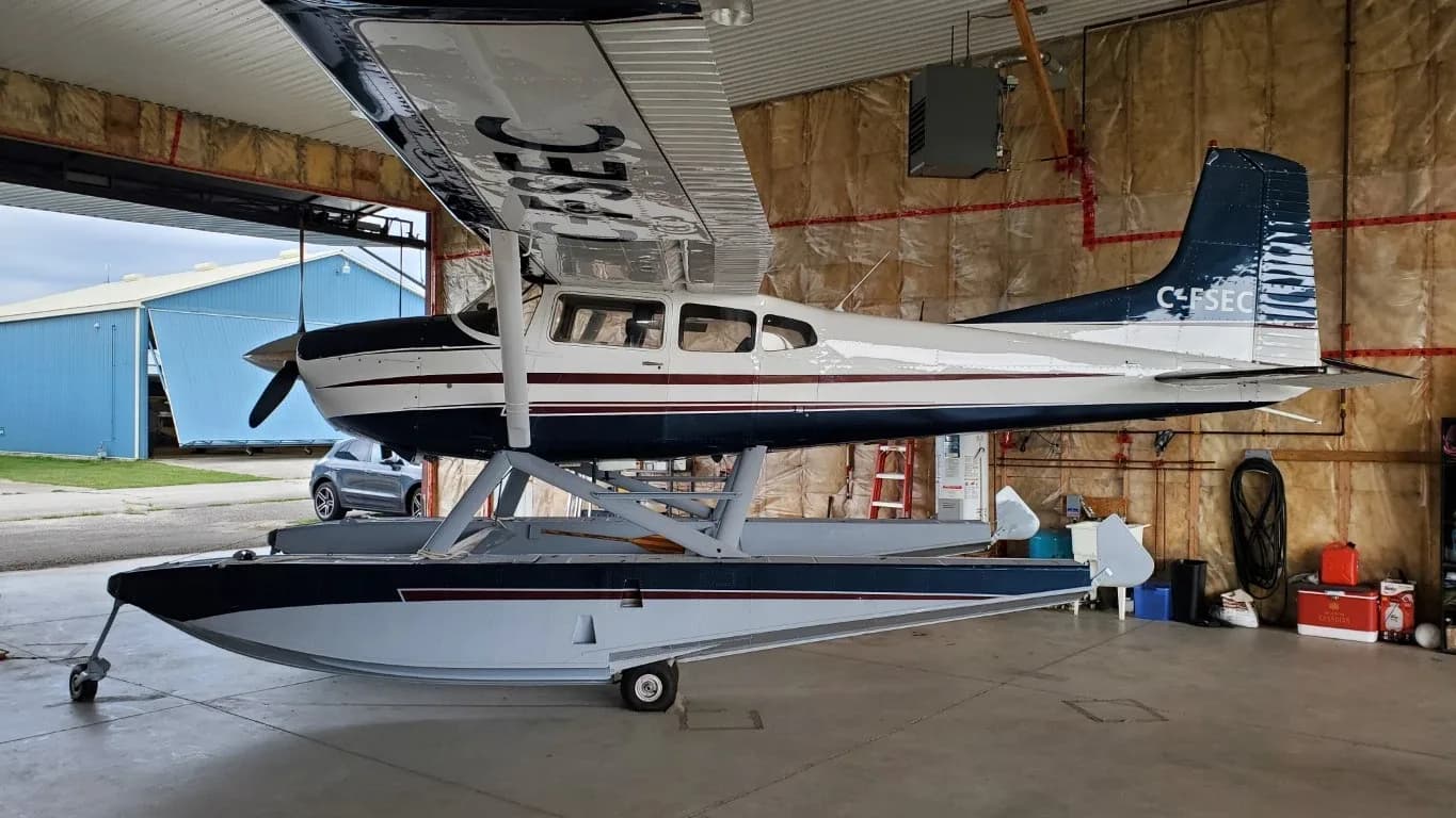 A white and dark blue floatplane with a maroon stripe, registration C-FSEC, parked inside a hangar with the door open.