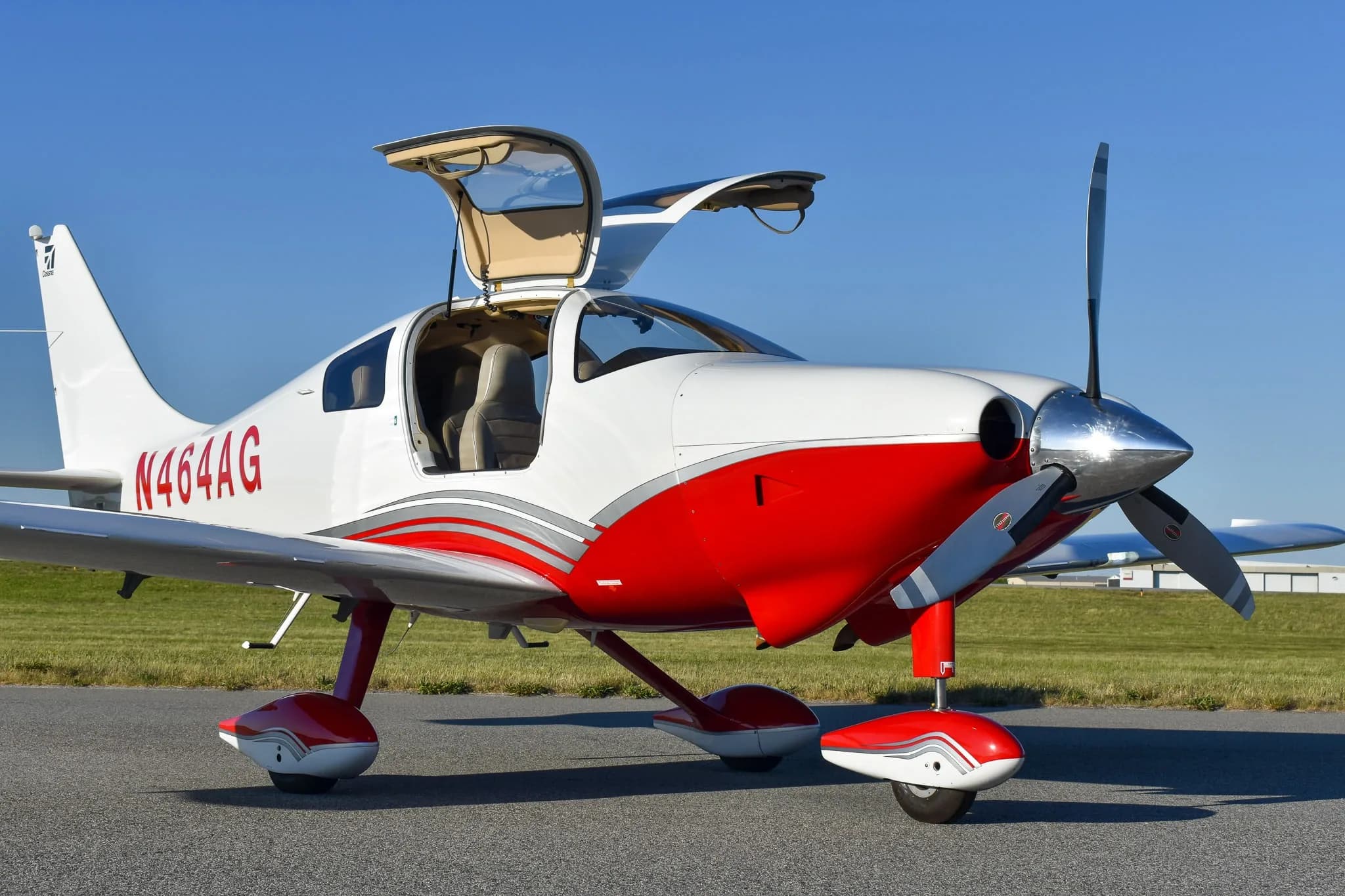 A white and red Cirrus SR22 aircraft, registration N464AG, with its gull-wing doors open, parked on an airfield.