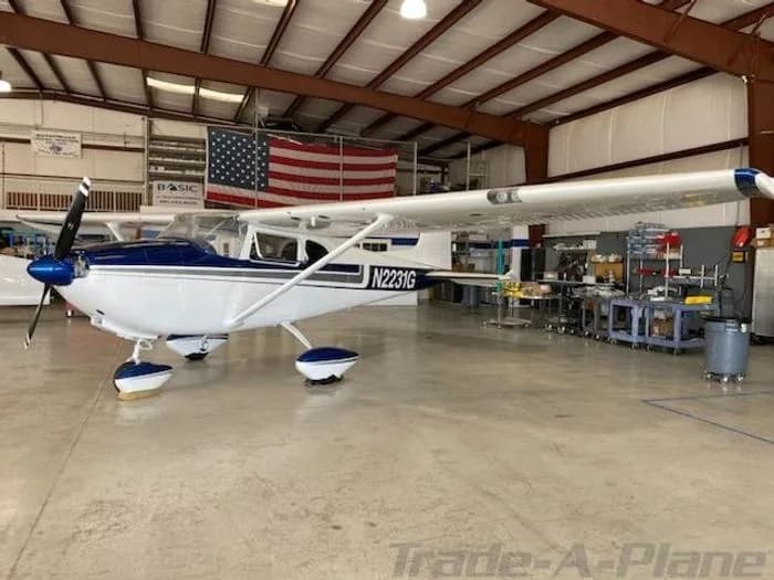 A white and blue single-engine, high-wing aircraft with registration N2231G is parked inside a hangar.