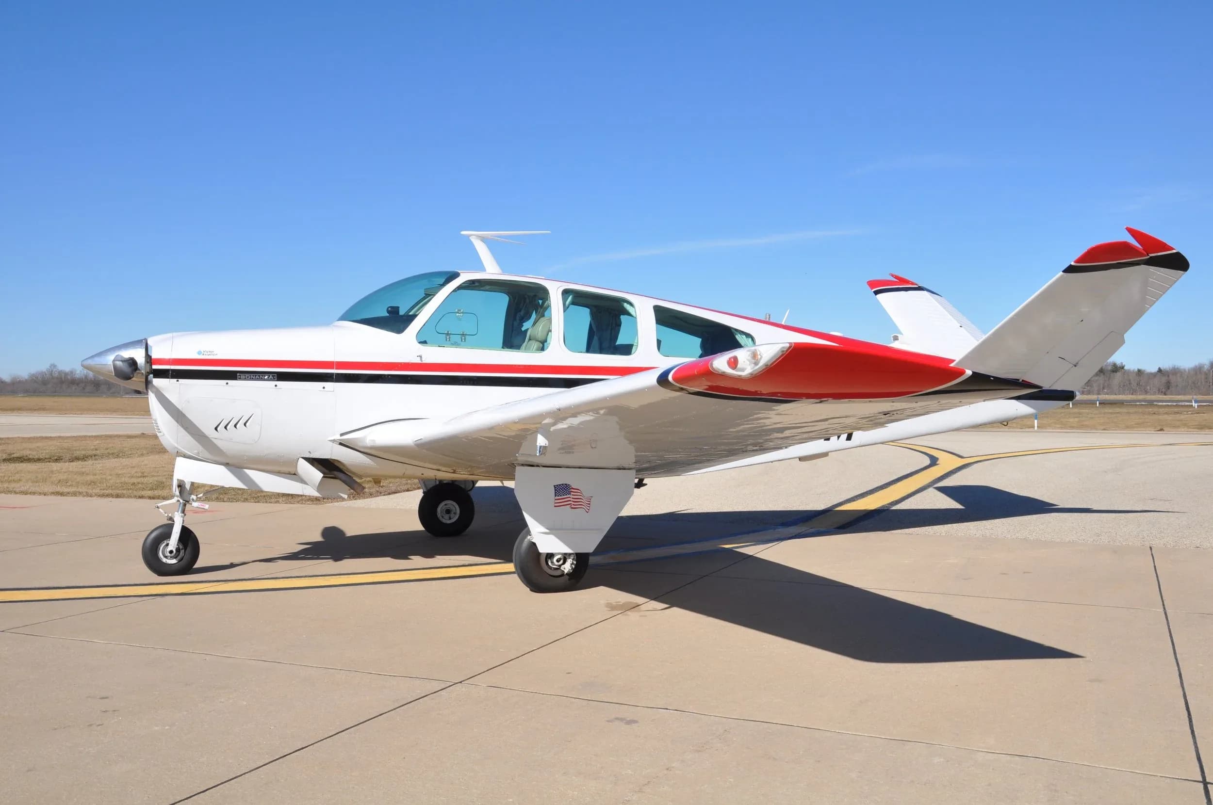A white and red single-engine aircraft is parked on a tarmac under a clear blue sky.