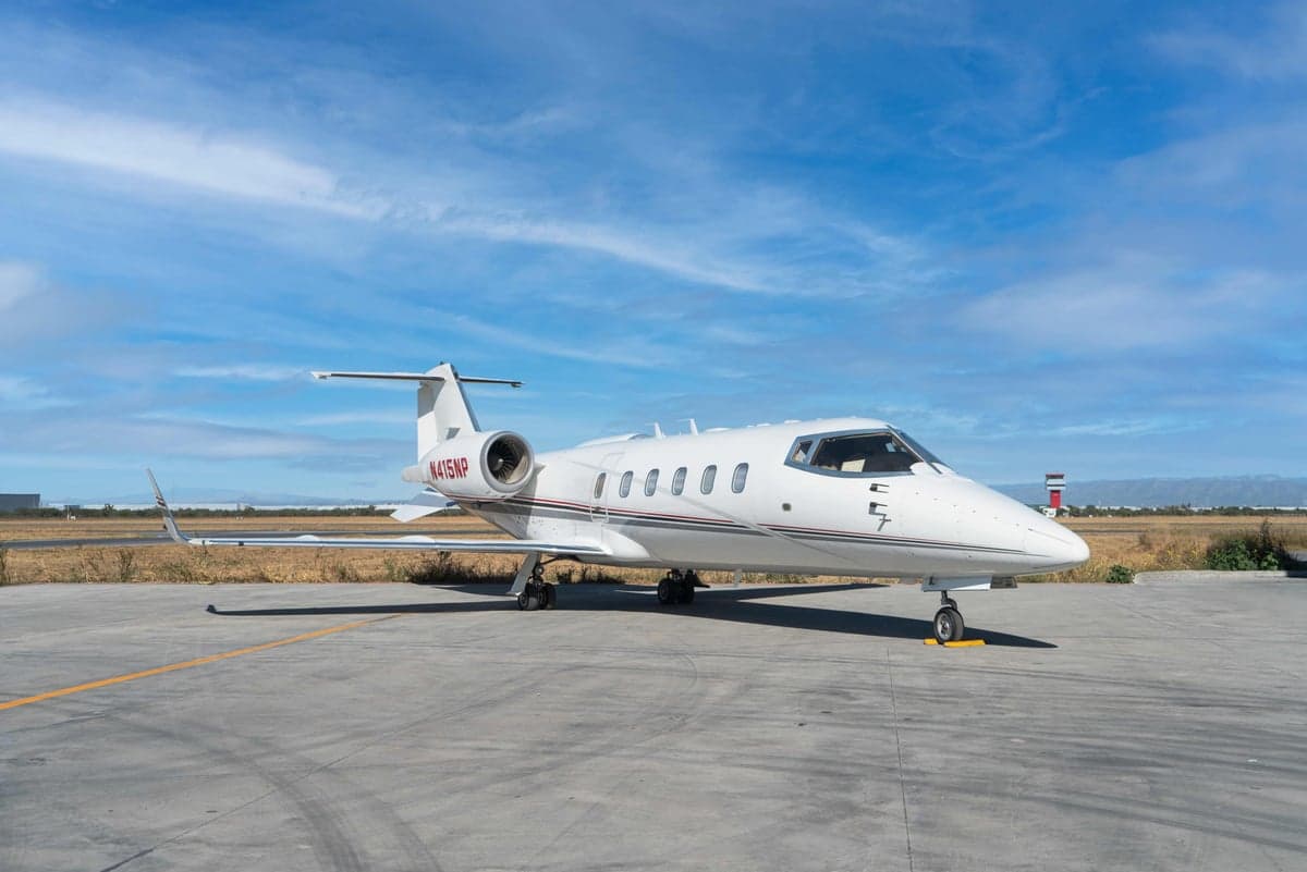 A white Learjet 45XR with registration N415NP is parked on the tarmac under a blue sky.