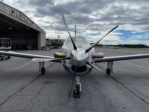Front view of a turboprop aircraft on the tarmac with a jet center in the background.