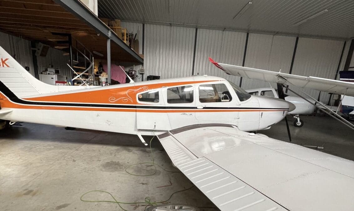 Side view of a white and orange aircraft with decorative swirls on the fuselage, parked in a hangar.