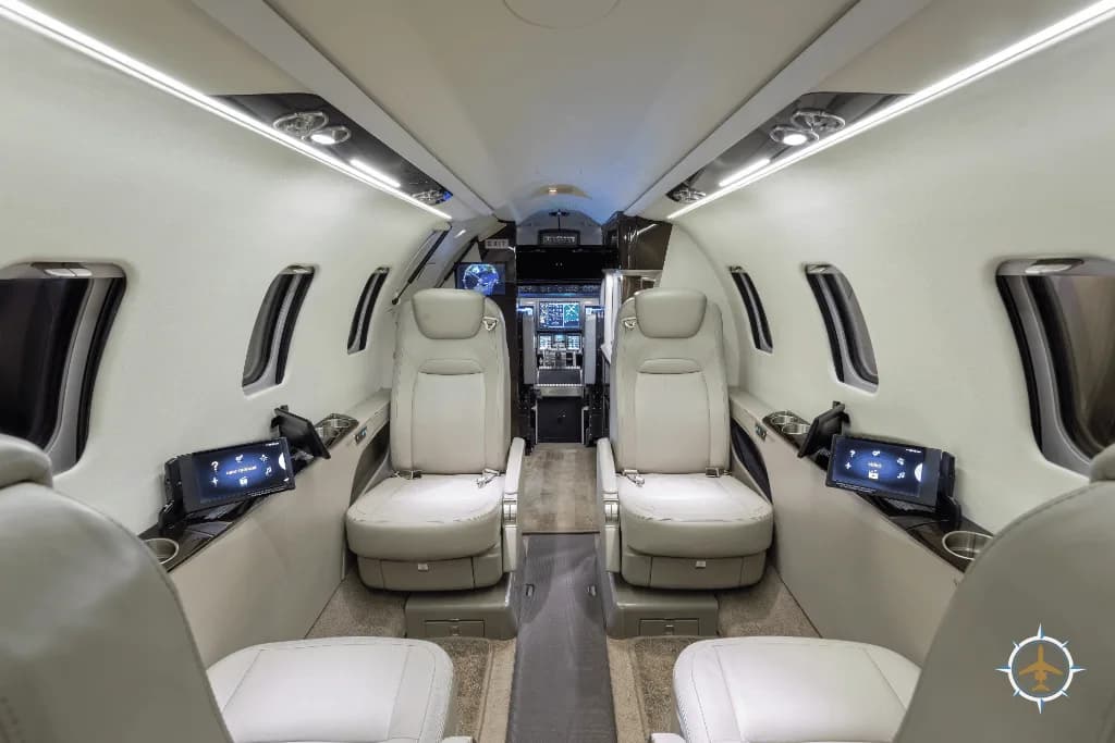 A private jet cabin with light-colored leather seats, individual screens, and cup holders on the side panels.