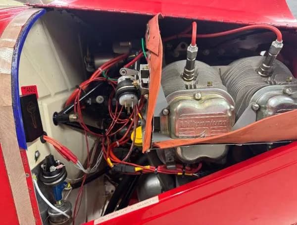 A close-up view of the exposed engine compartment of a red aircraft, showing Millennium cylinders and wiring.