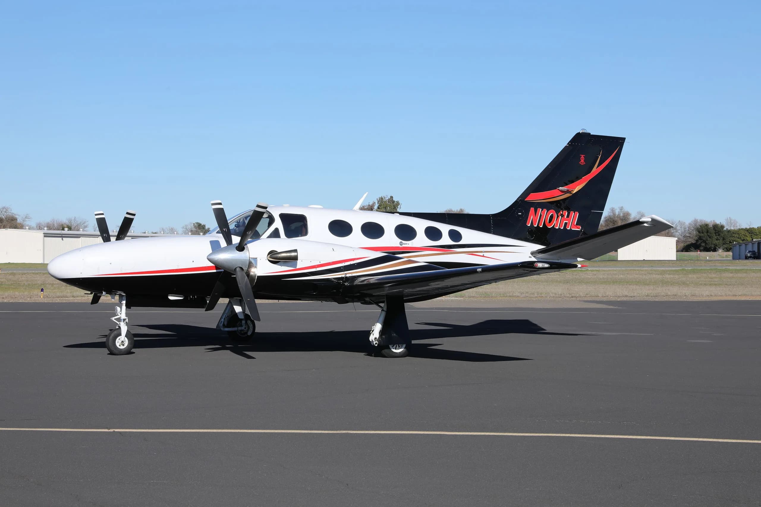 A three-quarter view of the white, black, and red Cessna 414 Chancellor parked on an asphalt tarmac.