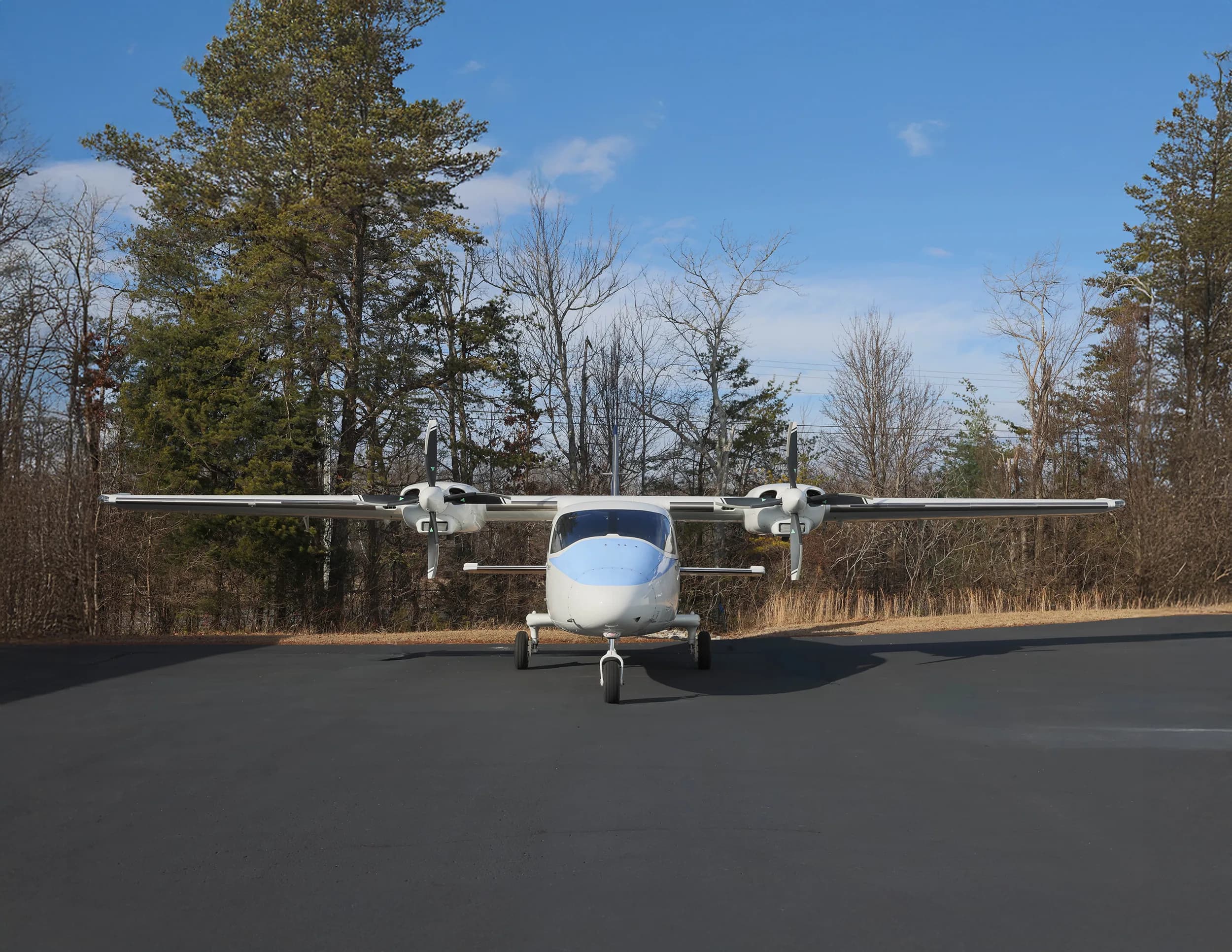 Front view of a white and blue twin-engine aircraft with two propellers, parked on an asphalt ramp.