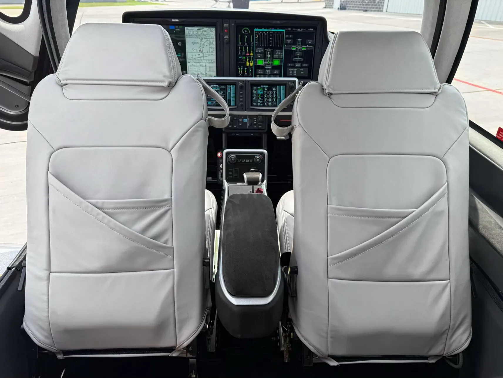 A view from the cabin into the cockpit, showing the white front seats and the digital instrument panel.