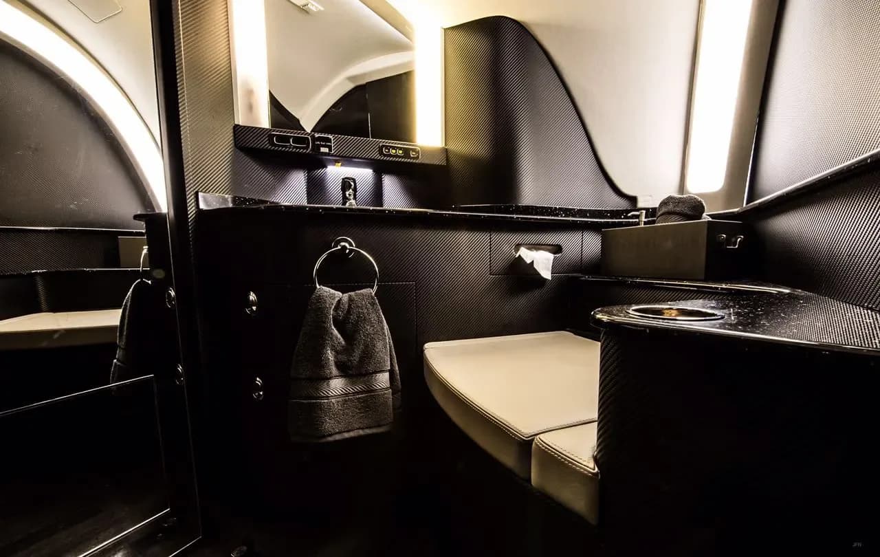 A modern aircraft lavatory with dark textured walls, a sink, and a toilet seat.